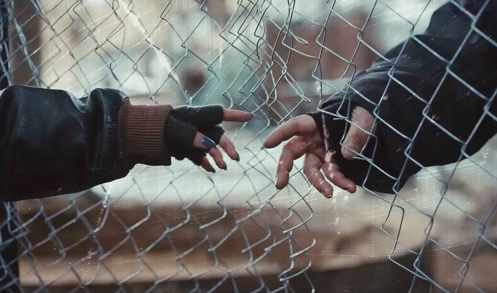 Две руки тянутся друг к другу через металлическую сетку